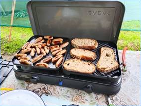 A grill with sausages and bread on it

Description automatically generated